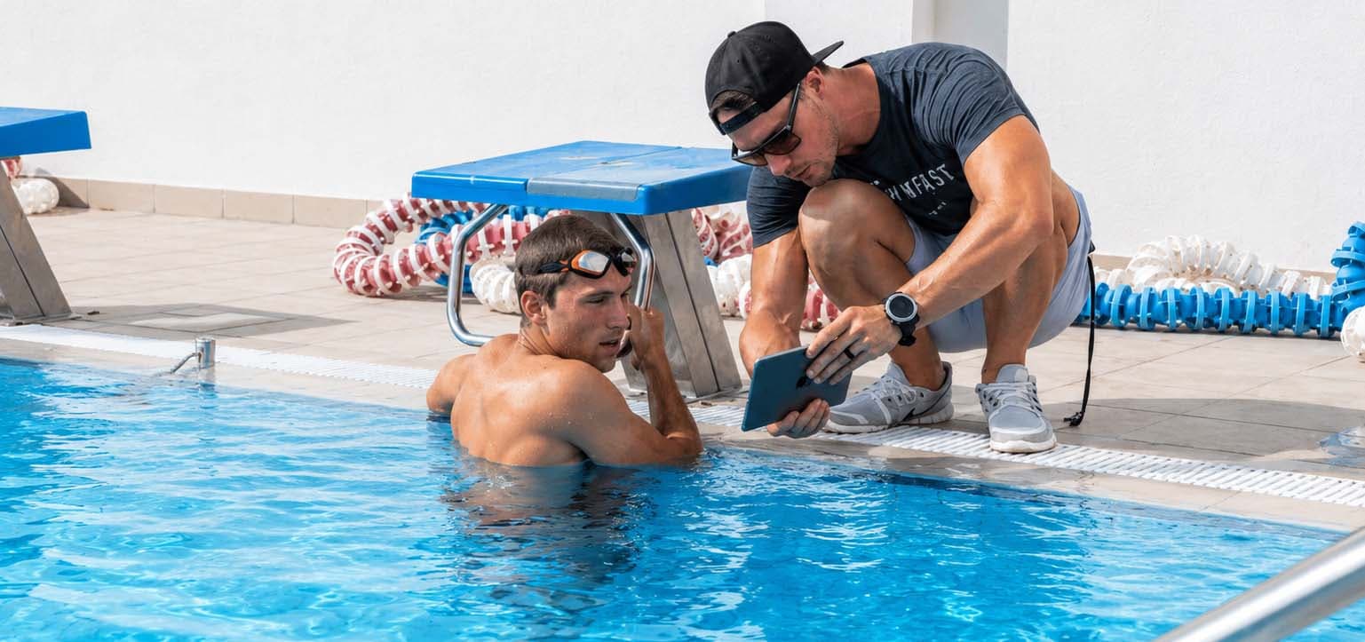 Coach reviewing swim technique on a tablet with an athlete at the pool